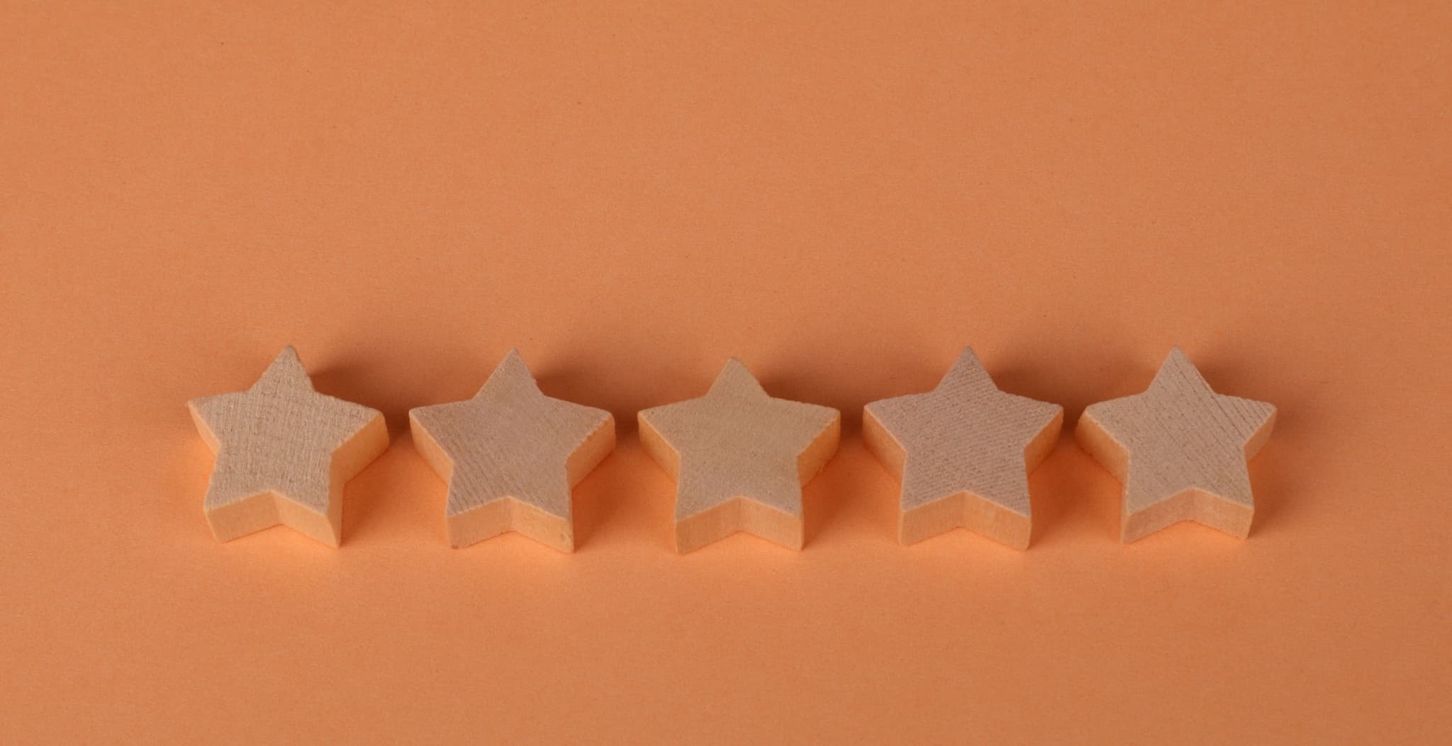 Five wooden star-shaped blocks lined up in a row on a warm orange background, a customer-rating concept shot with generous negative space above