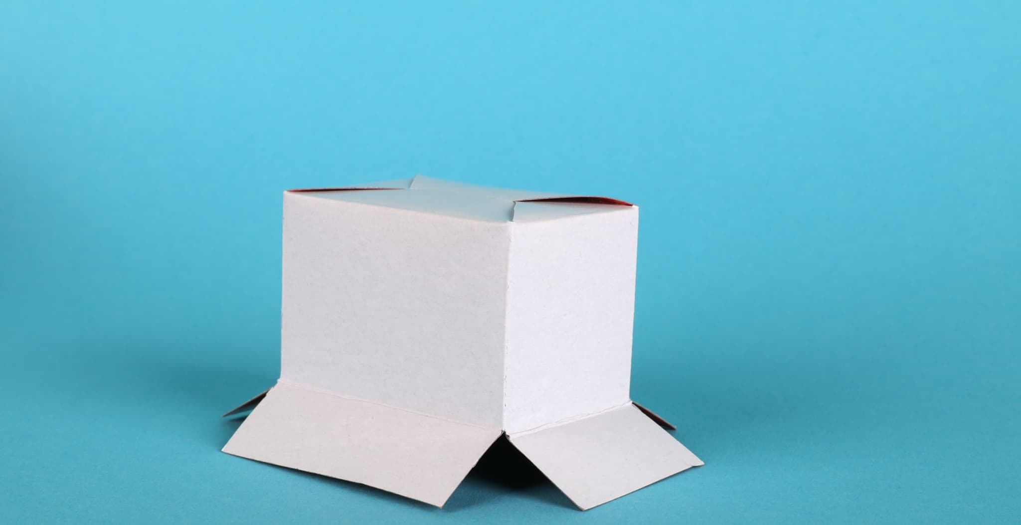 A small white cardboard shipping box with its top flaps open, sitting on a solid blue background.