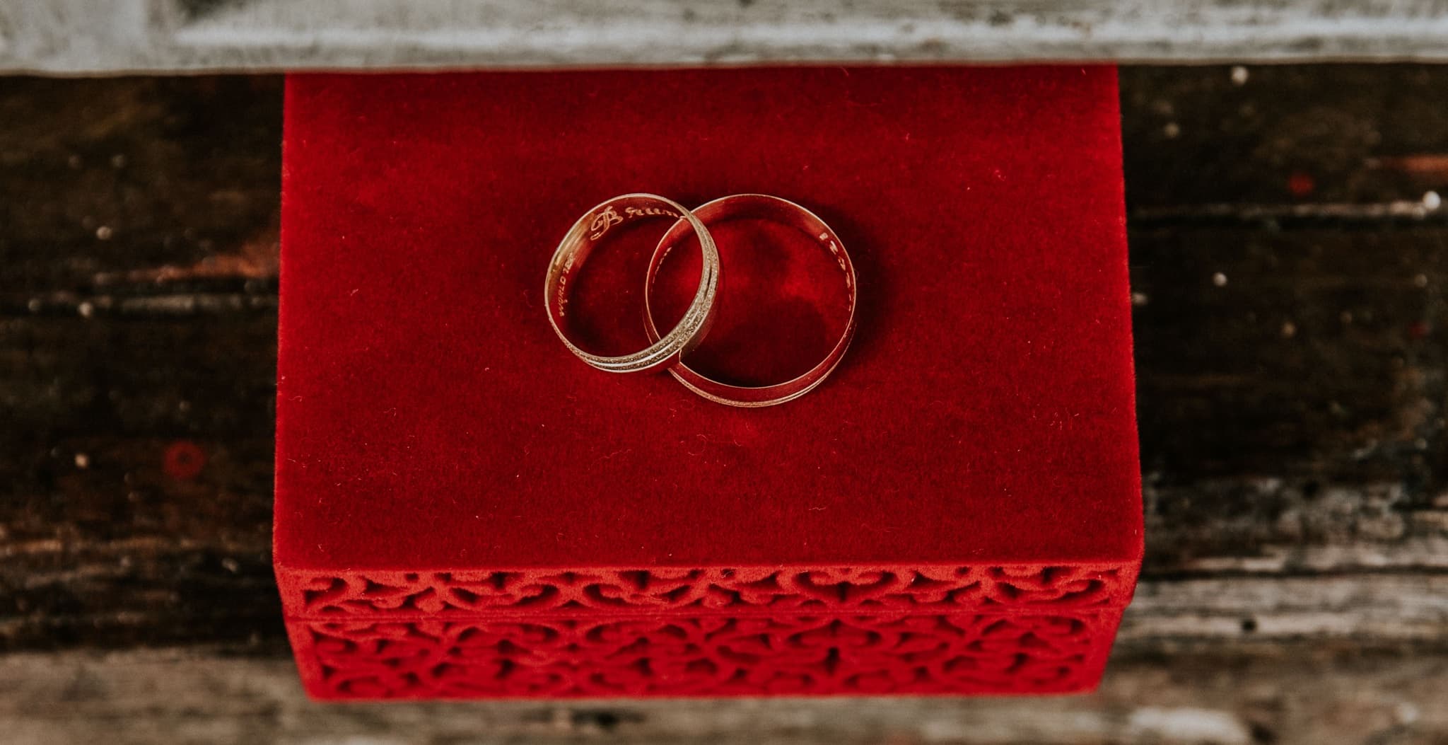Two interlocking gold rings resting on a red velvet box against a weathered wood surface.